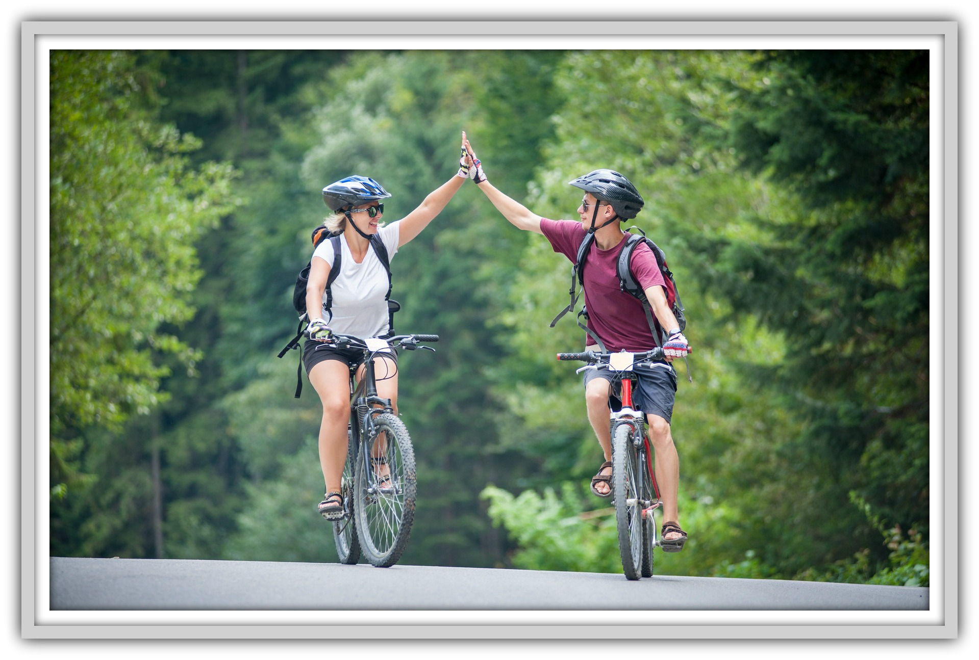 happy couple goes on a mountain asphalt road in the forest on bikes with helmets giving each other a high five